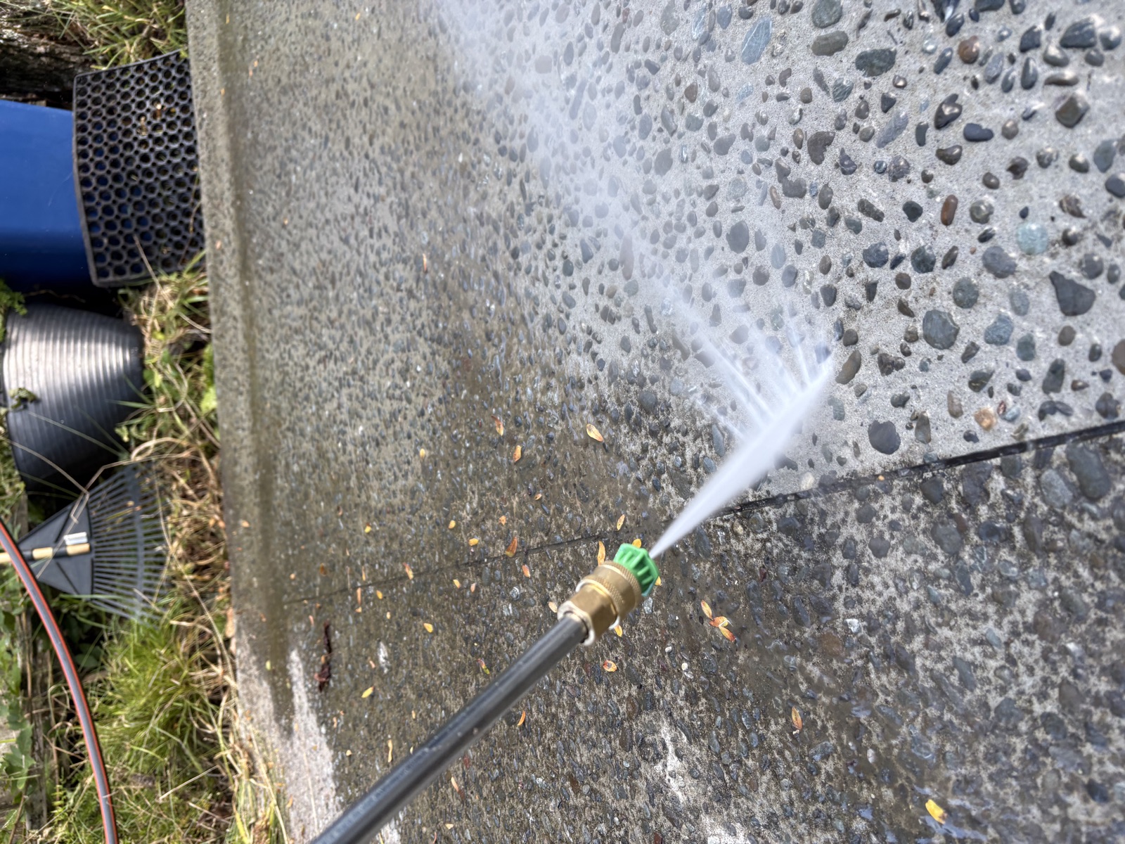 A pressure washer lance cleaning an exposed-aggregate concrete path, the cleaned strip visibly lighter